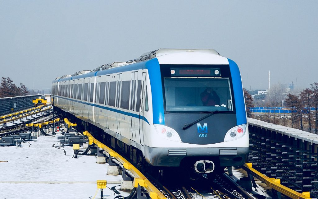 O trem da linha 1 do metrô de Wuhan na estação Jinghe. Trem azul com partes brancas de frente com neve nas laterais.