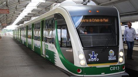 VLT em operação no Metrô de Teresina durante o dia, parado em uma estação com as portas fechadas. Na imagem, o trem é visto na diagonal, de frente. O veículo é branco com detalhes em verde. A estação tem teto em formato circular com uma abertura no alto que permite entrada de luz natural. Há uma pessoa de pé, do lado direito da imagem vestindo camisa clara e calça jeans. No letreiro do trem, pode-se ler "Governo do Estado do Piauí".