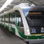 VLT em operação no Metrô de Teresina durante o dia, parado em uma estação com as portas fechadas. Na imagem, o trem é visto na diagonal, de frente. O veículo é branco com detalhes em verde. A estação tem teto em formato circular com uma abertura no alto que permite entrada de luz natural. Há uma pessoa de pé, do lado direito da imagem vestindo camisa clara e calça jeans. No letreiro do trem, pode-se ler "Governo do Estado do Piauí".